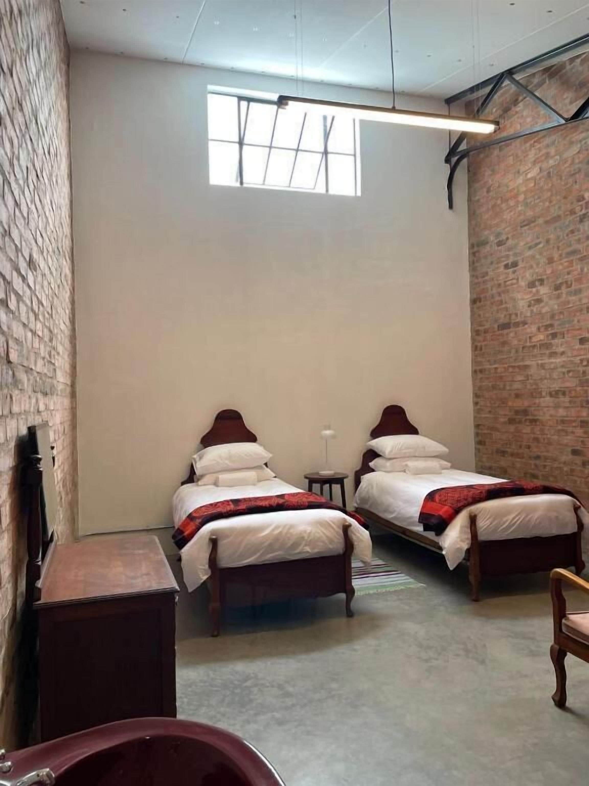A room with two wooden beds, a small table, a bench, and a brick wall.