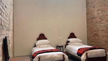 A room with two wooden beds, a small table, a bench, and a brick wall.