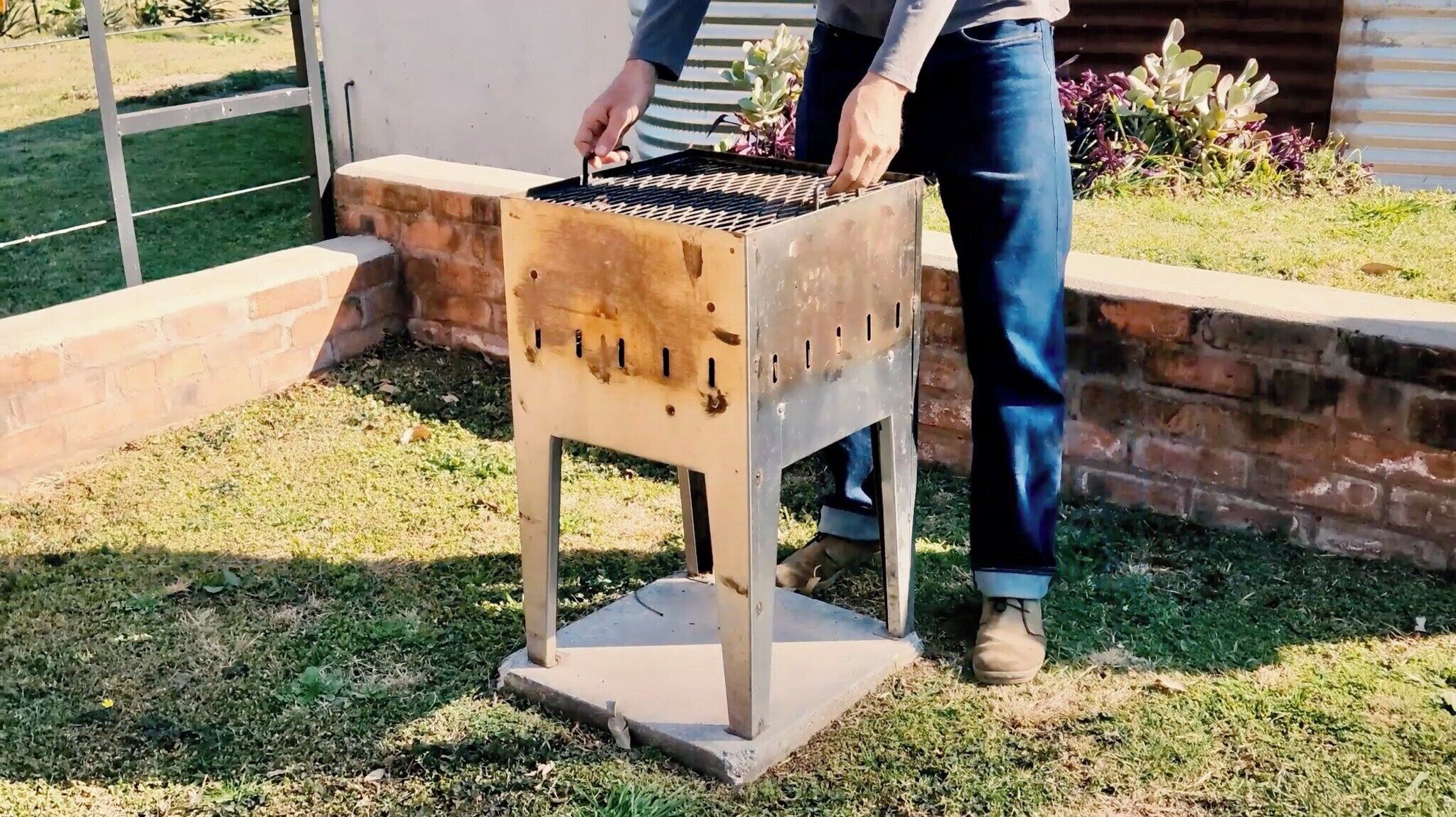 A person standing next to a metal barbecue grill outdoors.