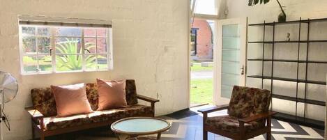 A room with a sofa, armchair, fan, and a patterned floor.
