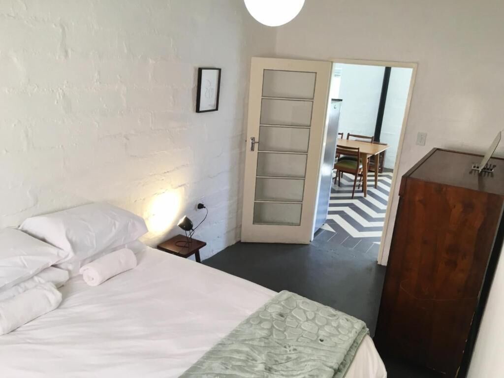 Une chambre à coucher comprenant un lit, une armoire en bois, une porte donnant sur un coin repas et un luminaire fixé au mur.