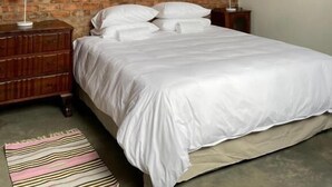 Una camera da letto con parete in mattoni, un letto con biancheria bianca, due comodini con lampade e un tappeto a righe.