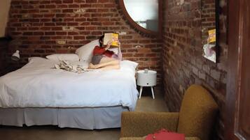 Un dormitorio con pared de ladrillo, un espejo redondo, una cama, una mesita de noche y una silla.