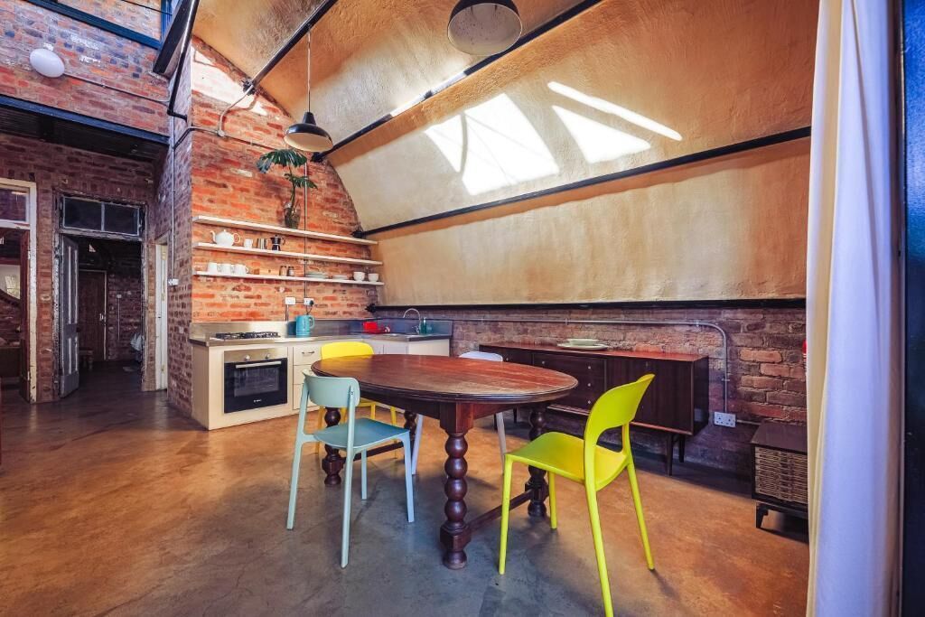 Una cocina con pared de ladrillo, una mesa redonda de madera y dos sillas.