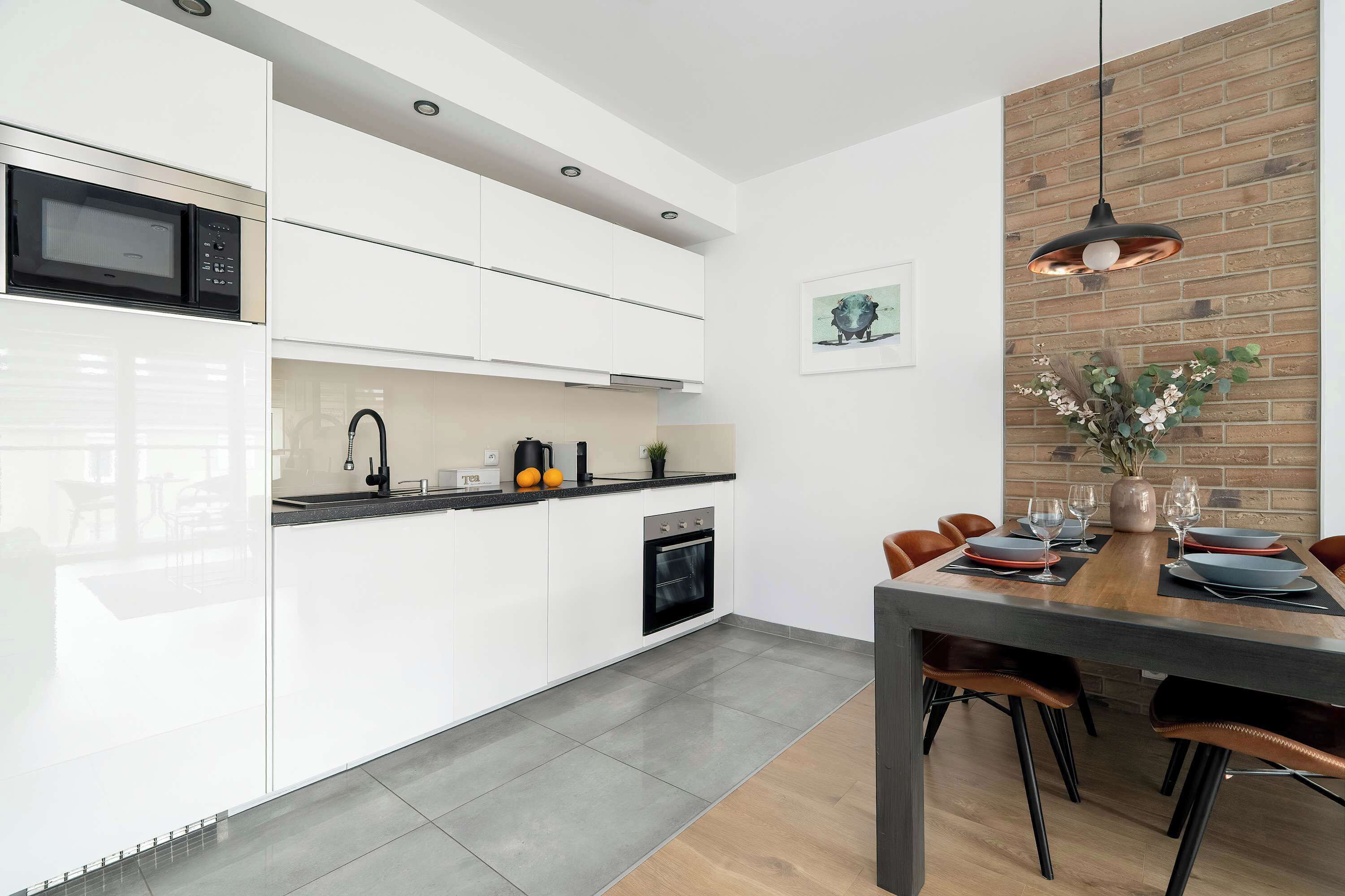 A modern kitchen with white cabinets, a built-in oven, and a dining area with a wooden table and chairs.