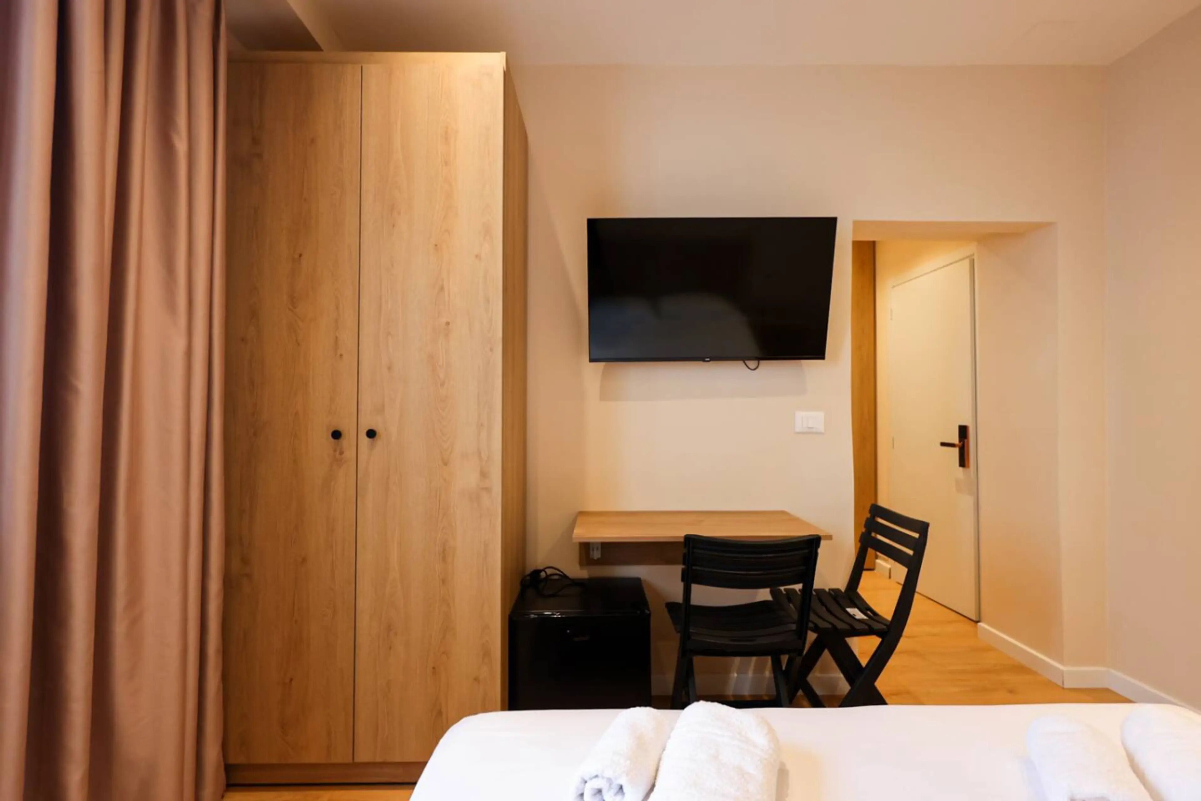 Un dormitorio con cama, escritorio, silla, armario y televisor montado en la pared.
