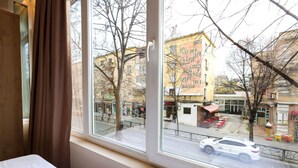 Una habitación con un ventanal grande que da a una calle con edificios y un coche estacionado.