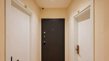 Um corredor com uma porta escura no final, paredes brancas e uma luminária no teto.