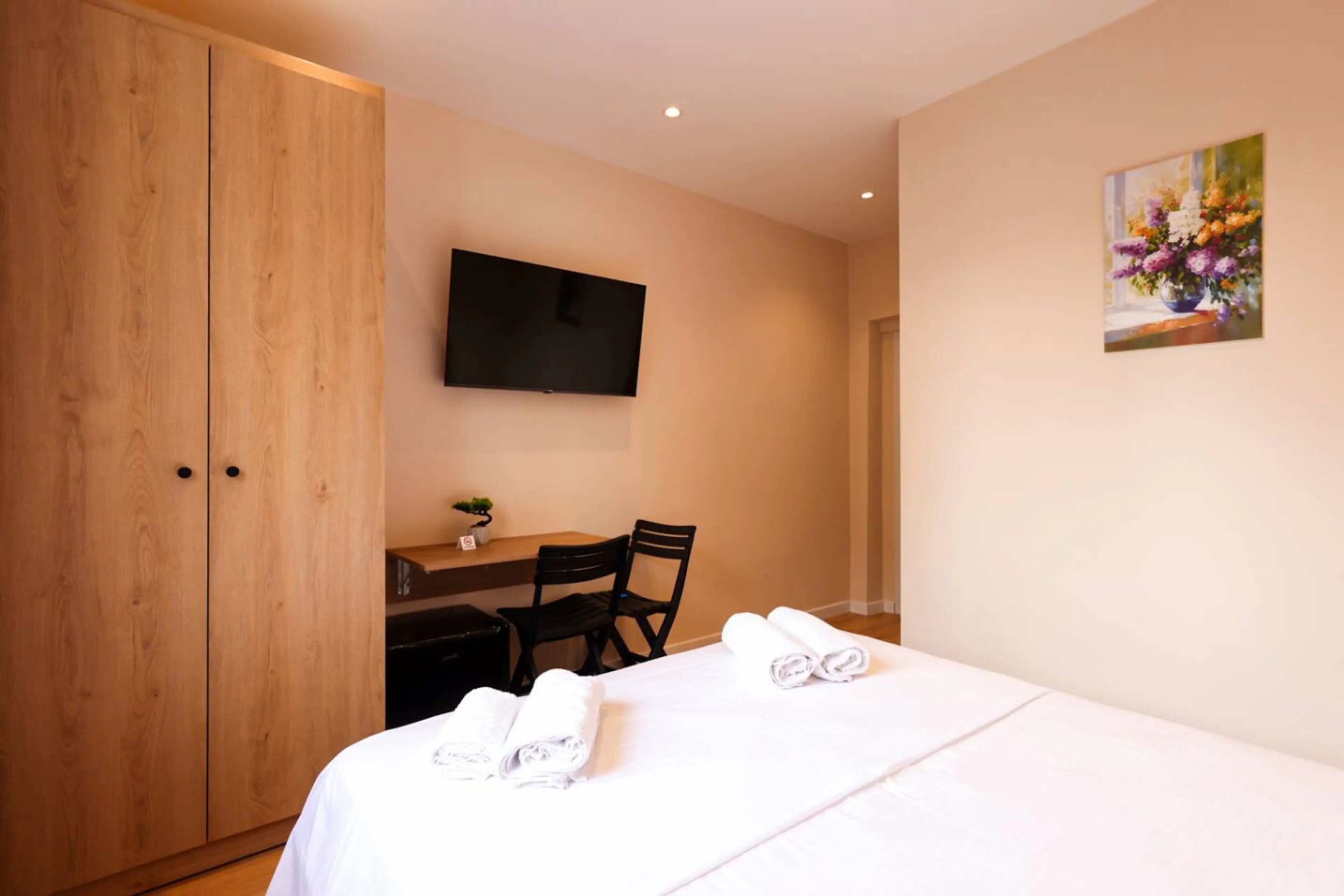 A hotel room with a bed, a desk with a chair, a television on the wall, and a painting.