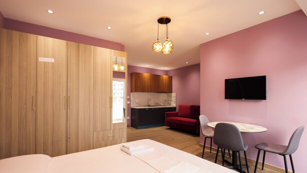 Habitación de hotel con cama, escritorio con sillas, televisor, sofá rojo y armario de madera.