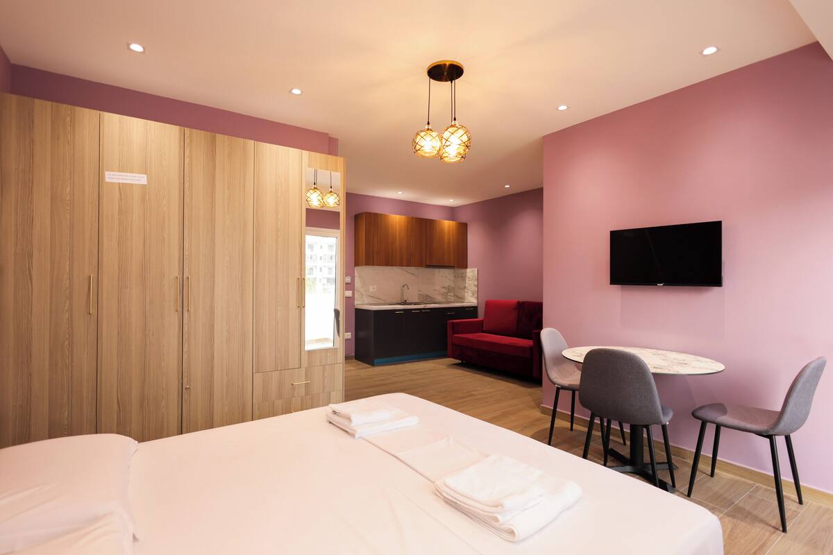 Habitación de hotel con cama, escritorio con sillas, televisor, sofá rojo y armario de madera.