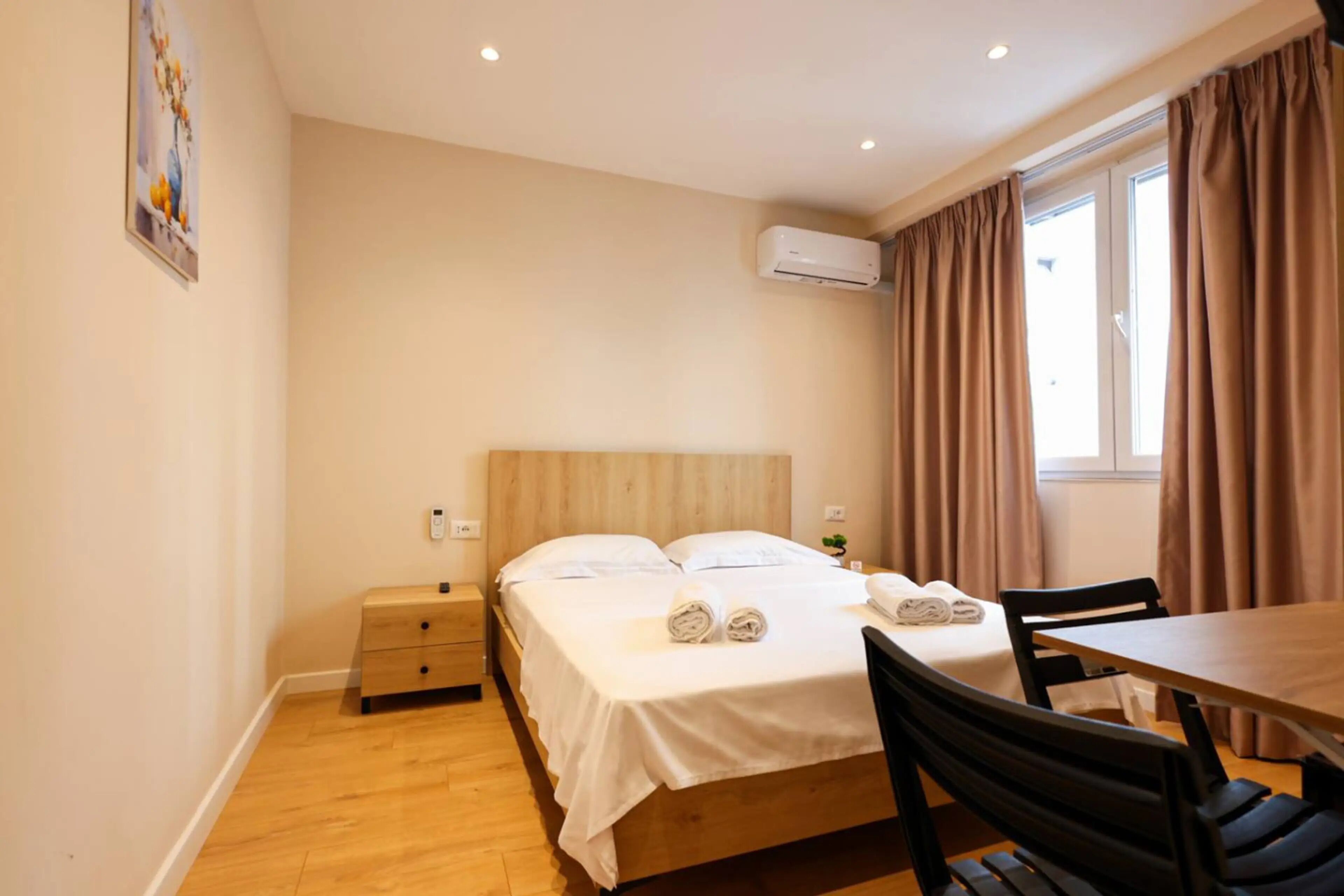 Habitación de hotel con cama, mesita de noche, silla y ventana con cortinas.