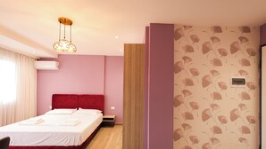 Habitación de hotel con cama, cabecera roja, suelo de madera, aire acondicionado montado en la pared y papel tapiz estampado.