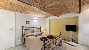 A bedroom with a brick ceiling, a bed with a headboard, a flat-screen TV, and a bedside table.