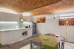 Une cuisine avec un plafond en briques, des armoires blanches, une table à manger avec des chaises et un tableau accroché au mur.
