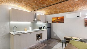 A compact kitchen with a sink, microwave, and stove, a dining table with chairs, and a brick ceiling.