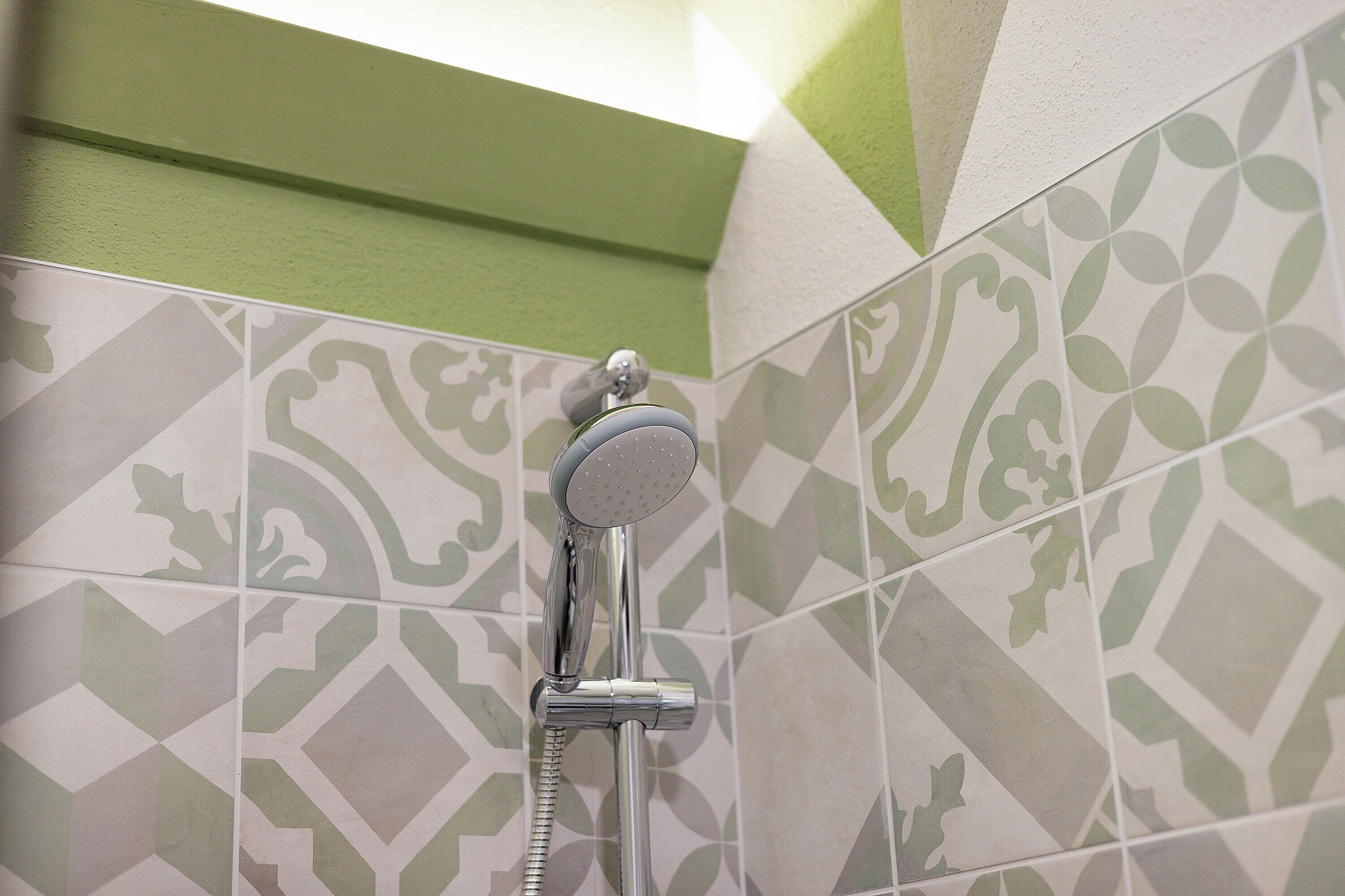 A shower with a handheld showerhead, a wall-mounted faucet, and patterned tiles.