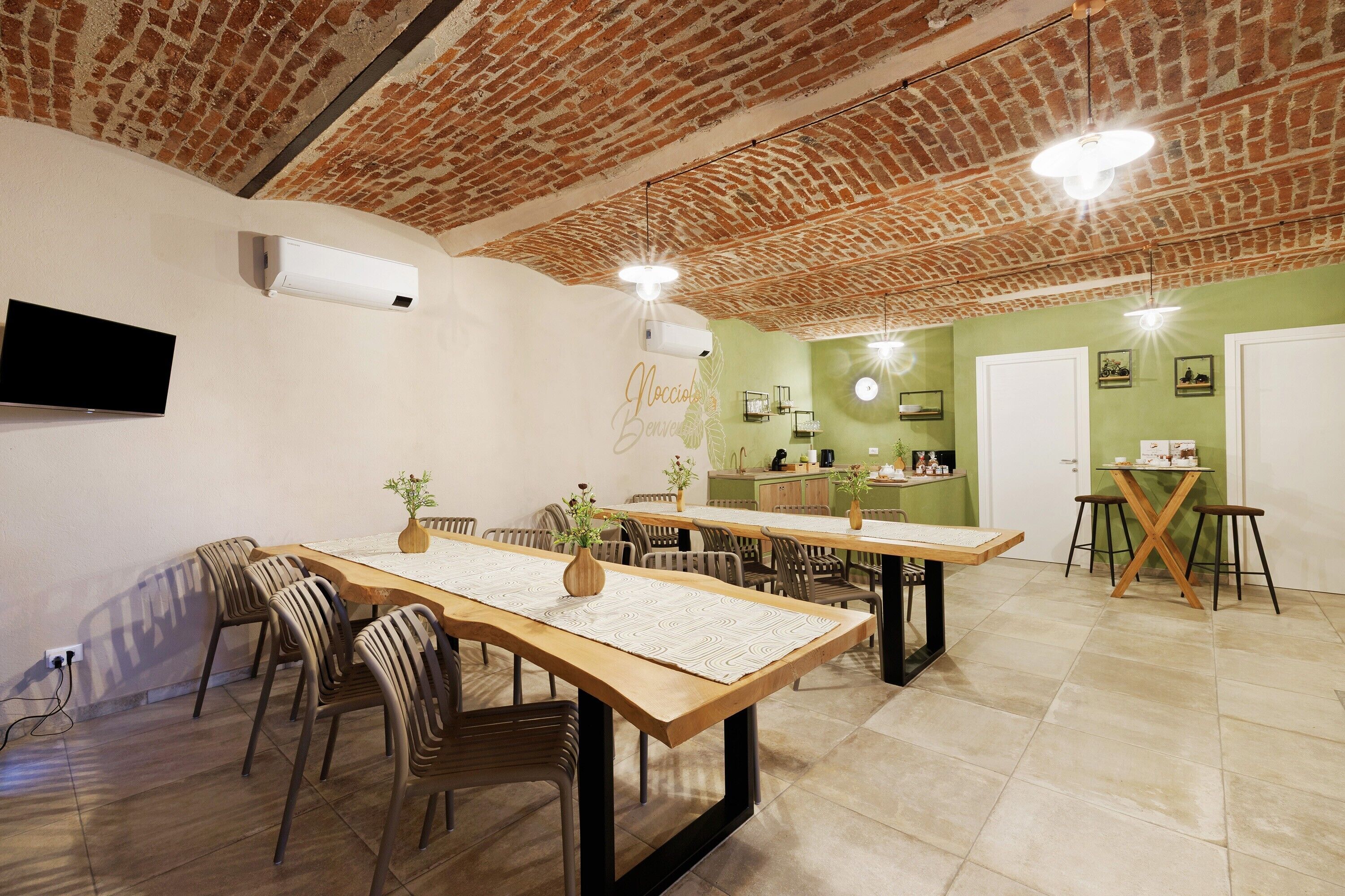 A dining area with brick ceiling, wooden tables, and chairs, and a green accent wall.
