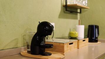 Une machine à café posée sur un plateau en bois, un verre, une théière jaune et une cafetière noire sur un plan de travail.