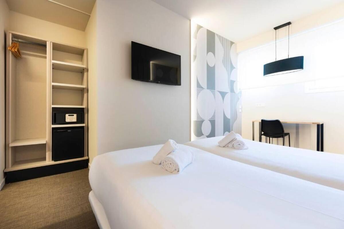 Ein Hotelzimmer mit zwei Betten, einem Fernseher, einem Schreibtisch und einem Kleiderschrank.