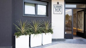 A building entrance with a window, a sign reading 'INDUSTRIAL AIA,' and three white planters with plants. - Urbaia Rooms (San Sebastian)