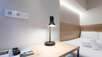 A hotel room with a bed, a desk with a lamp, a remote control, and a brochure.