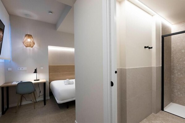 Una habitación de hotel moderna con escritorio, silla, cama y zona de ducha.