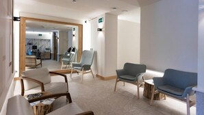 A modern hotel lobby with seating areas, a reception desk, and a visible exit sign. - Urbaia Rooms (San Sebastian)