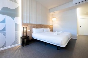 A modern hotel room with a large bed, a bedside table, a wall-mounted light, and a door. - Urbaia Rooms (San Sebastian)