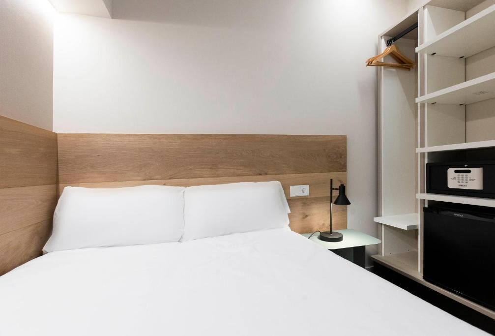 A hotel room with a bed, a nightstand, a lamp, a wardrobe, and a built-in TV.