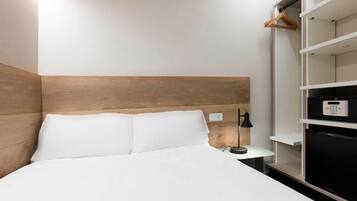 A hotel room with a bed, a nightstand, a lamp, a wardrobe, and a built-in TV.