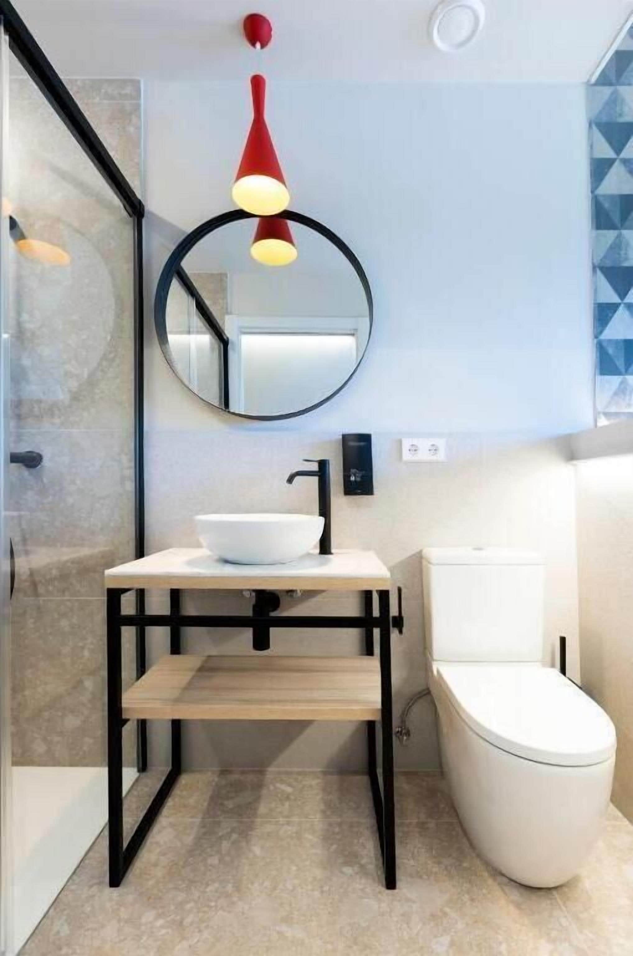 A modern bathroom with a white sink, black frame, and a red pendant light.