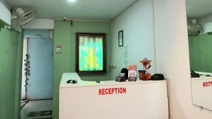 Ett entréområde med en receptionsdisk märkt med texten ”RECEPTION”, ett väntrum med en soffa och en dörr som leder till ett rum med en säng.