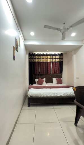 A bedroom with a bed, curtains, a ceiling fan, and a chair. - The Human Stay (Indore)