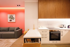 Una cocina moderna con encimera blanca, horno y armarios, una mesa de comedor con sillas y un sofá gris en la sala de estar.