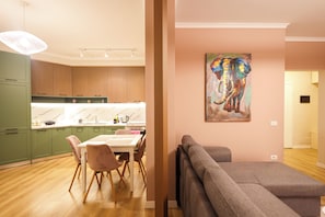 Una cocina moderna con armarios de madera, una mesa de comedor con sillas y un sofá gris en una sala de estar con un cuadro de un elefante.
