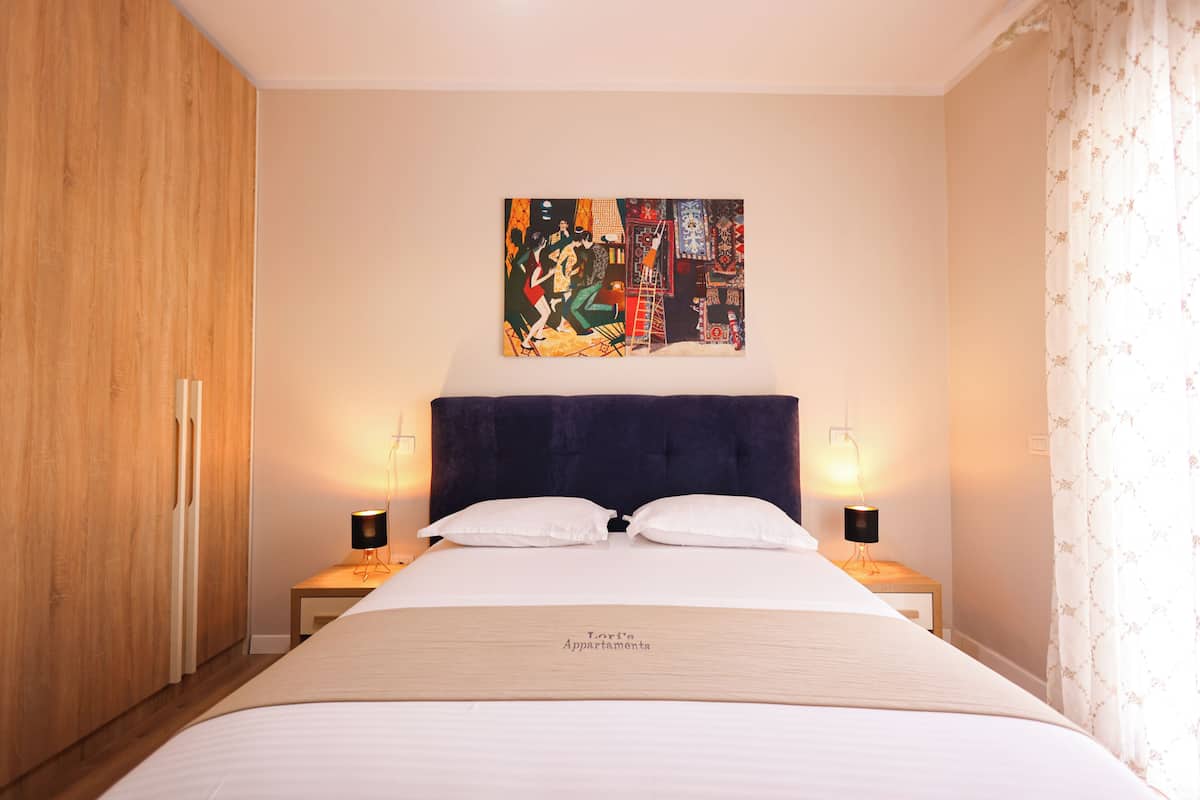 Quarto de hotel com uma cama grande, duas mesas de cabeceira, um quadro na parede e um guarda-roupa.