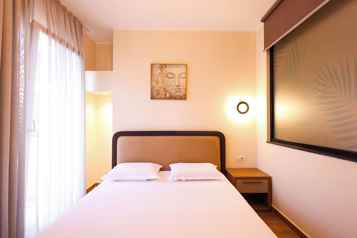 Quarto de hotel com cama, mesa de cabeceira, luminária na parede e um quadro.