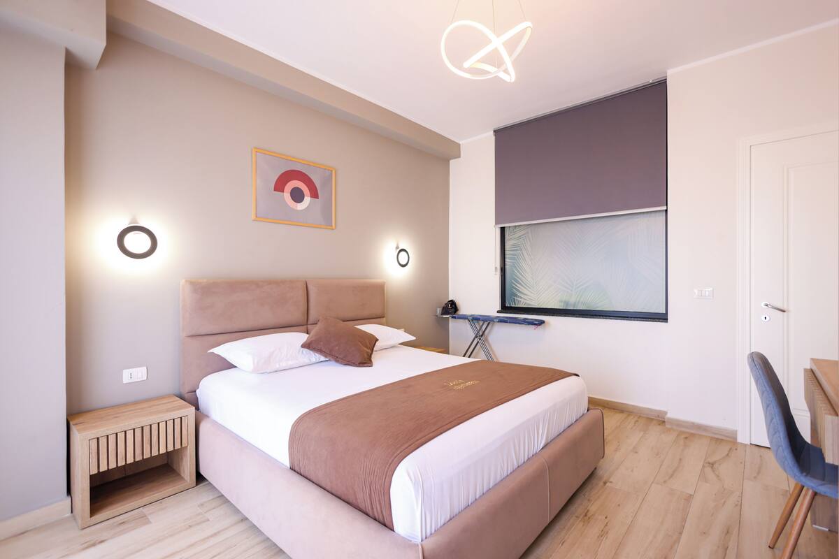 Quarto moderno com cama, mesa de cabeceira e janela com persianas.