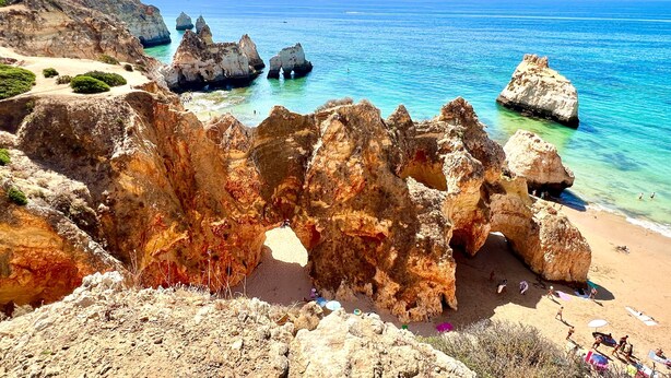 Un paysage côtier caractérisé par des formations rocheuses, une mer d’un bleu limpide et une plage de sable.