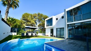 Une maison moderne dotée d’une piscine, d’un espace salon extérieur et d’une pelouse bien entretenue.