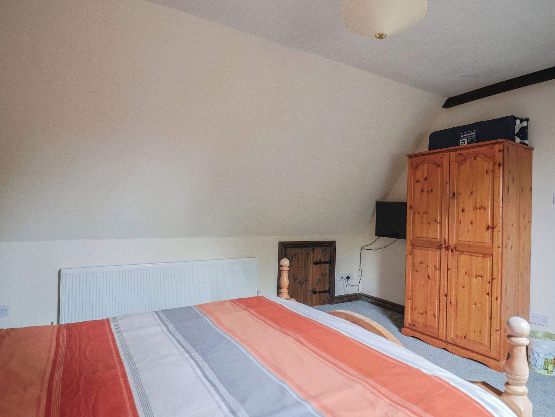 A bedroom with a bed, a wooden wardrobe, a radiator, and a television on the wall.