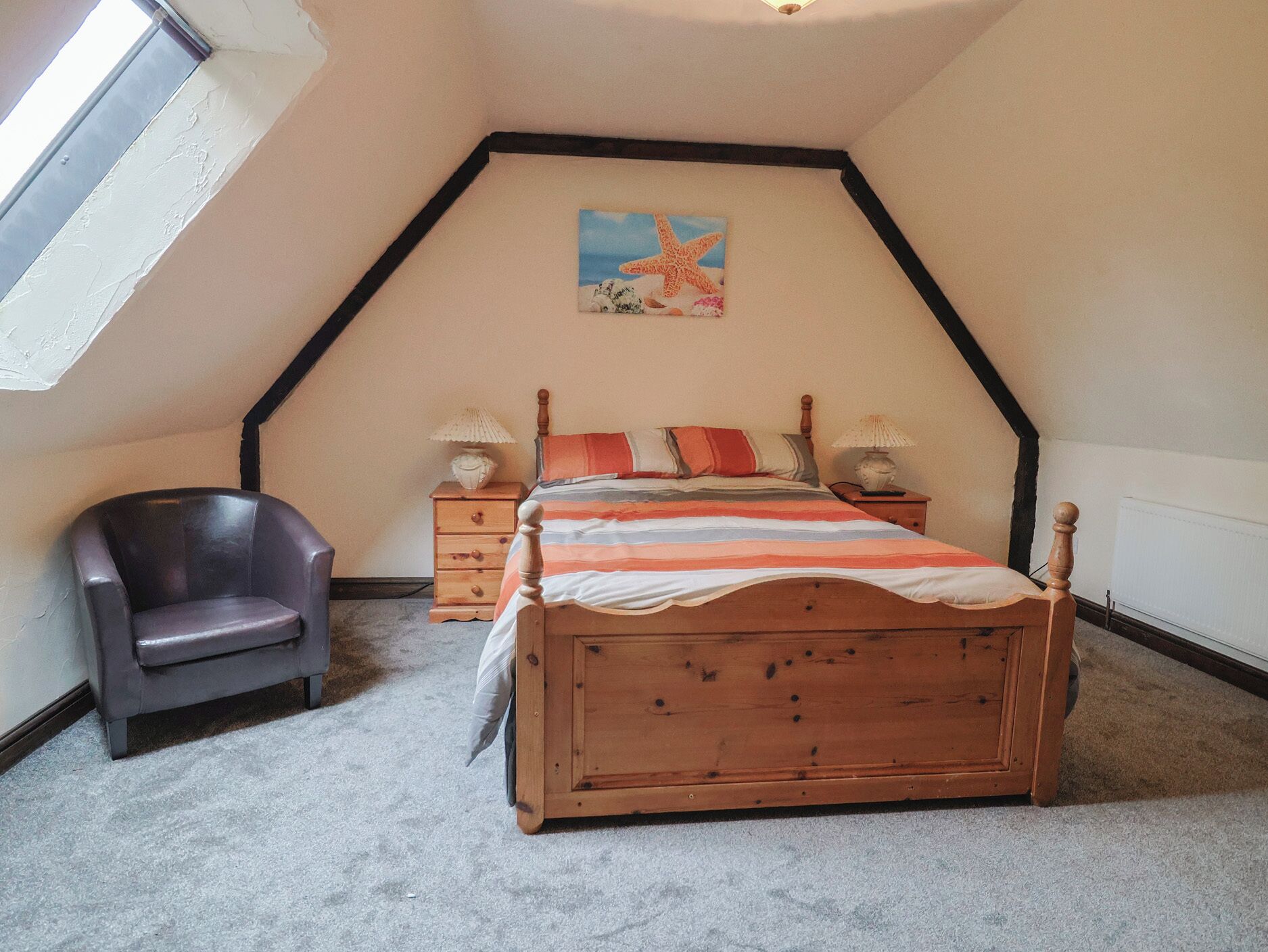 Un dormitorio con techo inclinado, una cama de madera, una mesita de noche, una silla y un cuadro con una estrella de mar.
