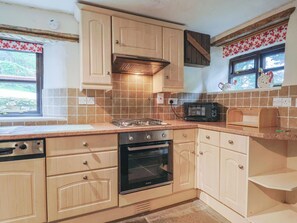 A kitchen with beige cabinets, a microwave, a stove, and a window with a floral curtain. - Cider House - Near Lyme Regis (Axminster)