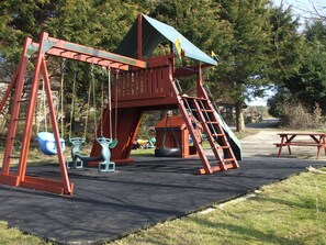 Ein Spielplatz mit Schaukeln, einer Rutsche und einem Picknicktisch.