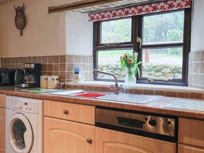 Eine Küche mit Waschmaschine, Kaffeemaschine, Spüle und einem Fenster mit Blick auf Grünflächen.