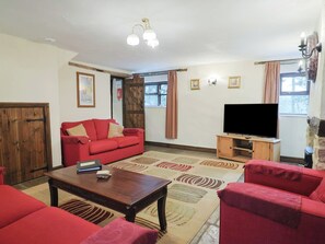 A living room with a red sofa, a wooden coffee table, a TV on a wooden stand, and a patterned rug. - Cider House - Near Lyme Regis (Axminster)