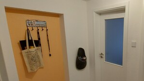 Un passadís amb una porta, un calaix per a sabates fixat a la paret i un sac penjant.