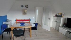 Un espai vital compacte amb zona de dinar, cuina americana, televisió i porta que dona a una altra habitació.