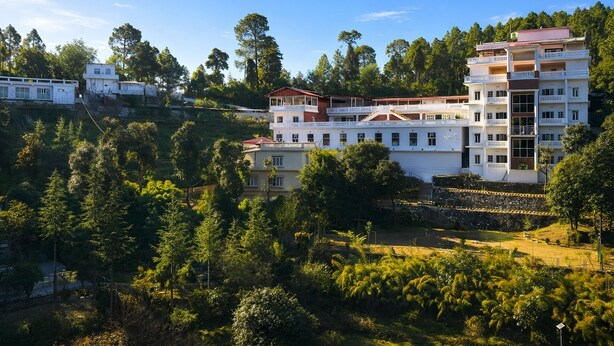 A multi-story building with balconies, surrounded by dense greenery and trees. - DLS Tehri Club Resort (Tehri)